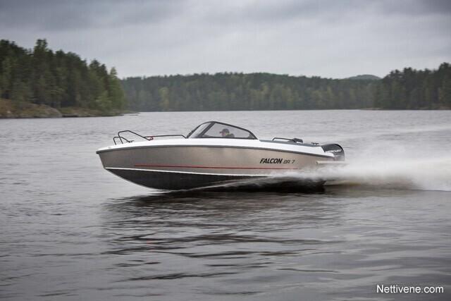 A Falcon 18 R speedboat glides across a calm lake, surrounded by lush green trees under a cloudy sky.